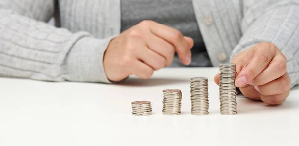 mujer está sentada en la mesa y una pila de monedas sobre la mesa. Cálculo de gastos e ingresos, subsidio, impuestos - Foto, imagen