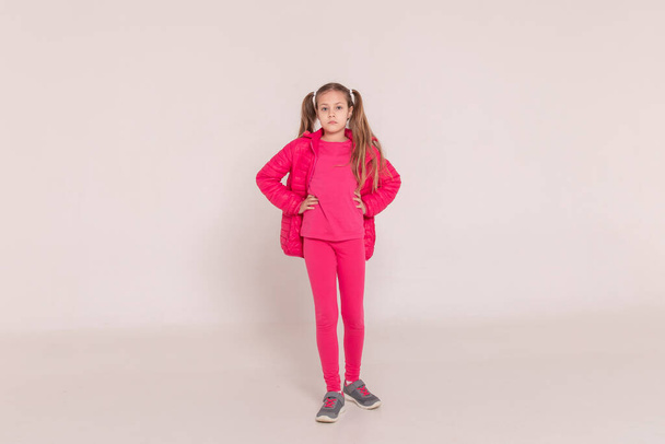 a girl with tails on a white background. baby in a pink jacket. Copy space - Фото, изображение