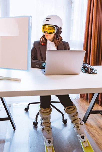 женщина в лыжном снаряжении работает на ноутбуке в офисе мечтая о зимних каникулах - Фото, изображение