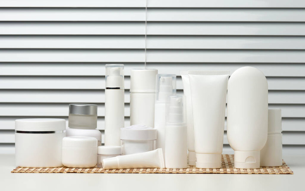 白いテーブルの上に化粧品用の瓶と空の白いプラスチックチューブ。クリーム、ゲル、血清、広告や製品のプロモーションのためのパッケージ、モックアップ - 写真・画像