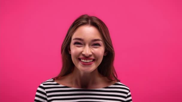 veselá žena v pruhované košili s dlouhým rukávem se směje na kameru izolované na růžové - Záběry, video