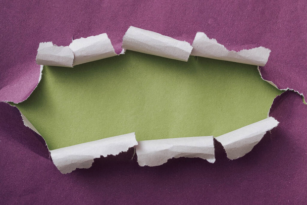 Zerrissener oder zerrissener lila Papierrahmen mit gewellten Kanten und grünem Kopierraum, der hinten in einer langen ovalen Form offenbart wird - Foto, Bild