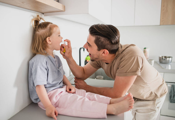 Young father taking care of his little daughter indoors at home, applying medication. - Photo, image