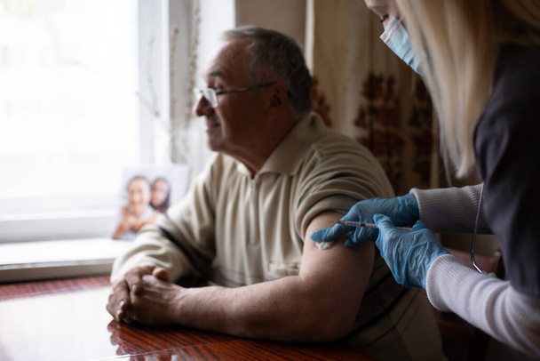 Mujer joven médico inyectando la vacuna al hombre anciano durante la visita domiciliaria - Foto, Imagen