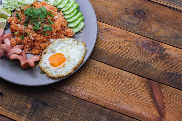 Американский жареный рис подается с сосисками, огурцами, измельченными овощами в серой тарелке на столе с приправами в Таиланде. - Фото, изображение