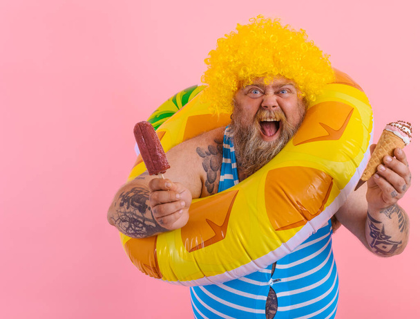 Grasso uomo con barba e parrucca mangia un ghiacciolo e un gelato - Foto, immagini