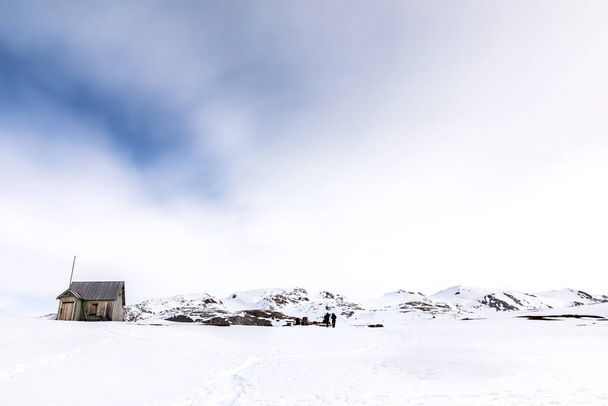 Cabaña abandonada y mina de mármol en Camp Mansfield, New London, Svalbard. Escena montañosa nevada con fotógrafos capturando el paisaje. - Foto, imagen