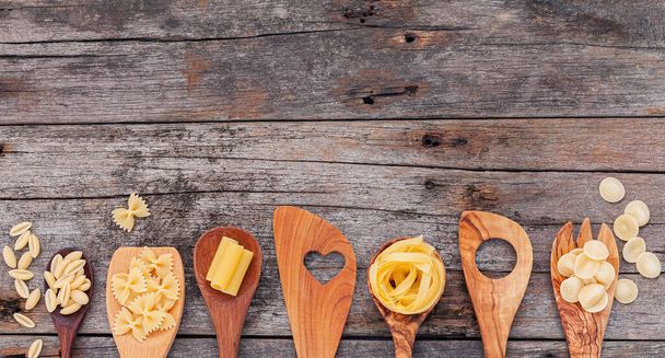 Italiaans voedselconcept en menuontwerp. Diverse soorten pasta elleboog macaroni, farfalle, rigatoni, gnocco sardo in houten lepels setup op houten achtergrond. - Foto, afbeelding