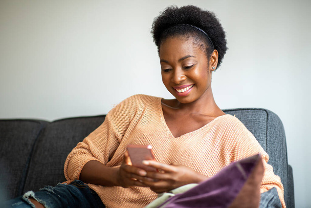 Retrato joven mujer negra sentada en casa mirando el teléfono móvil - Foto, Imagen