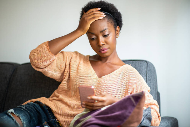 Portrait worried young black woman looking at mobile phone at home - Foto, Imagem