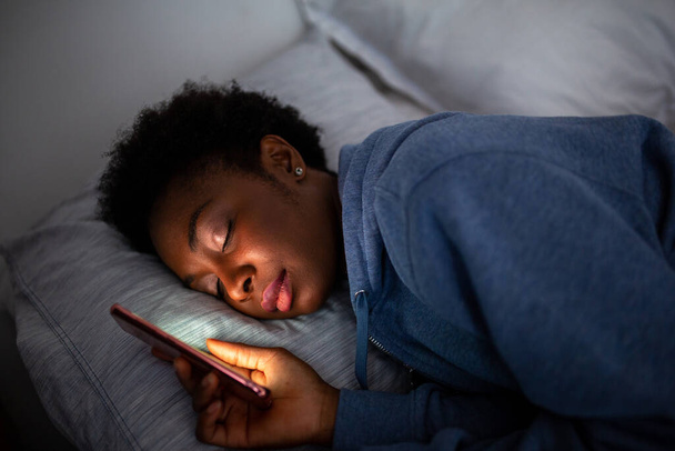 Close up portrait African American woman holding mobile phone and sleeping - Photo, image