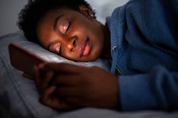 携帯電話を保持しながら眠っているポートレート疲れアフリカ系アメリカ人女性を閉じます - 写真・画像