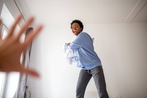 Portrait carefree young black woman in bedroom pillow fight - Fotoğraf, Görsel