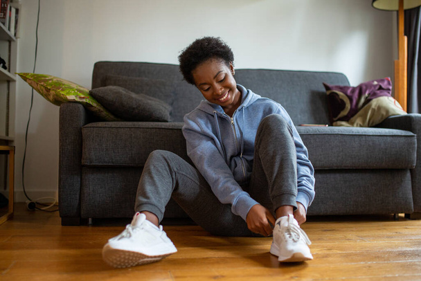 Portrait young African American woman siting on floor and putting on shoes - Foto, Bild