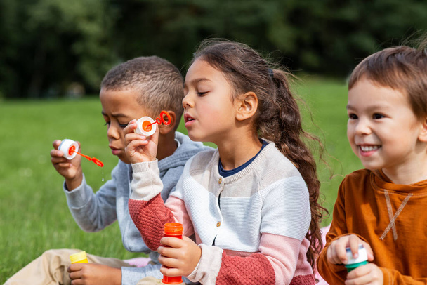 group of children blowing soap bubbles at park - Фото, зображення