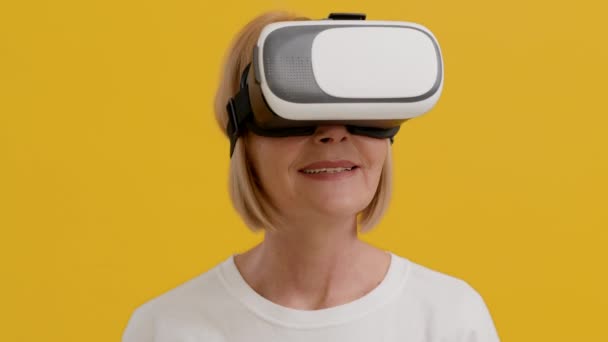 VRヘッドセットを装着した幸せなシニア女性が興奮して頭を回す - 映像、動画
