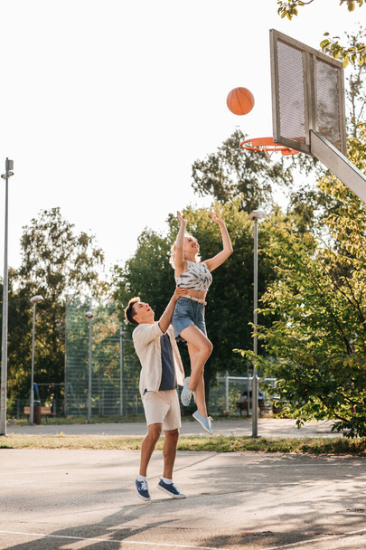 happy couple playing on basketball on playground - Foto, afbeelding