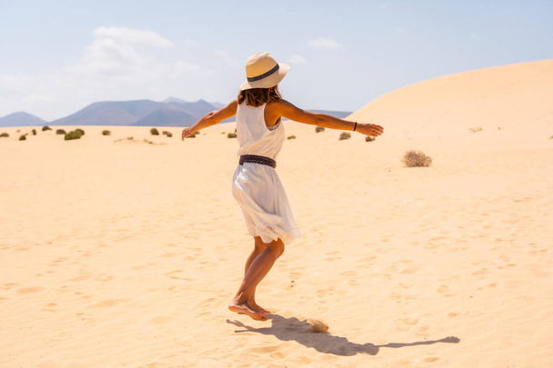 A young Caucasian tourist in a white dress and a hat walking through the dunes of the Corralejo Natural Park, Fuerteventura, Canary Islands. Spain - Photo, image