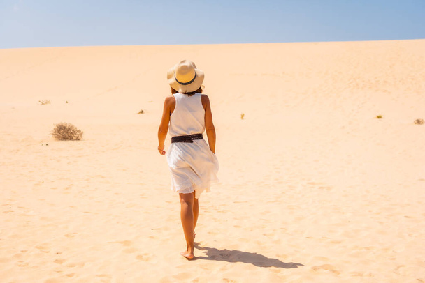 Tourist in white dress and hat walking through the dunes of the Corralejo Natural Park, Fuerteventura, Canary Islands. Spain - Фото, изображение
