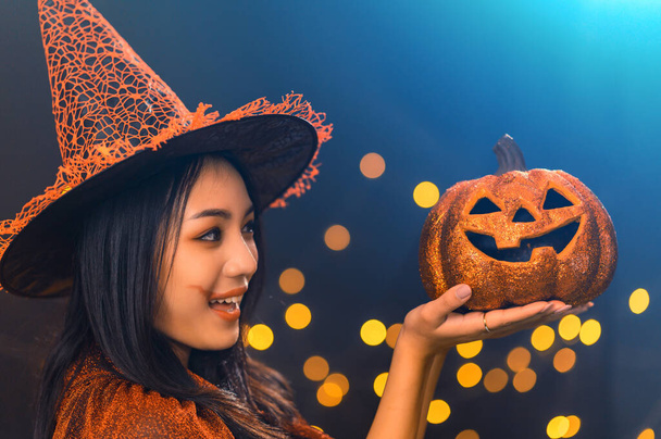 Titel: Portrait der schönen jungen Frau im Hexen-Halloween-Kostüm Hexenhut hält Kürbis Jack O Laternen über gruselig dunklen magischen Hintergrund - Halloween Party-Konzept - Foto, Bild