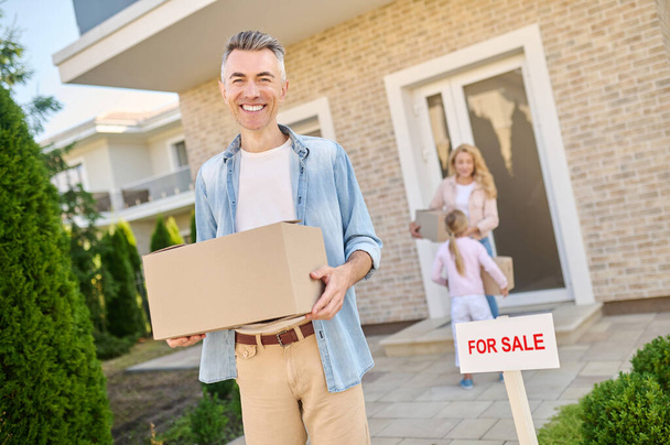 Smiling man taking the box out of house - Photo, image