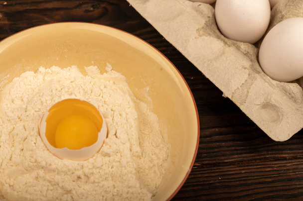 Zepsute białe jajko kurze w misce mąki pszennej i kilka pełnych jaj w tacce z białej tekturki, zbliżenie selektywne skupienie - Zdjęcie, obraz