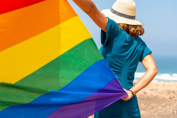 Lgbt symbol, an unrecognizable lesbian from the back in a green dress waving the flag by the sea - Фото, зображення