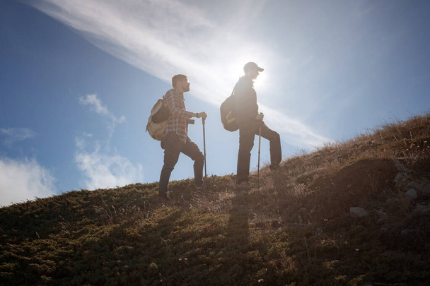 Two men silhouettes walking along the top of the mountain - Foto, Bild