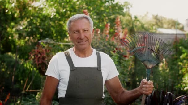 Schöner Senior Mann mit Laubrechen in der Hand posiert im Garten - Filmmaterial, Video