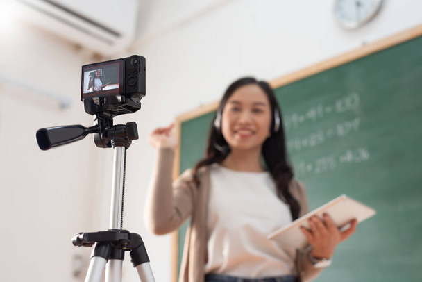 Selective focus, Smiling Asian Young woman teacher teaching and recording video with digital camera at front of blackboard. Live stream. - Фото, зображення