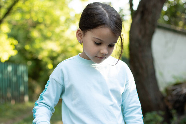 Маленькая красивая белая девочка улыбается смотрит вниз на размытый деревенский фон с боке - Фото, изображение