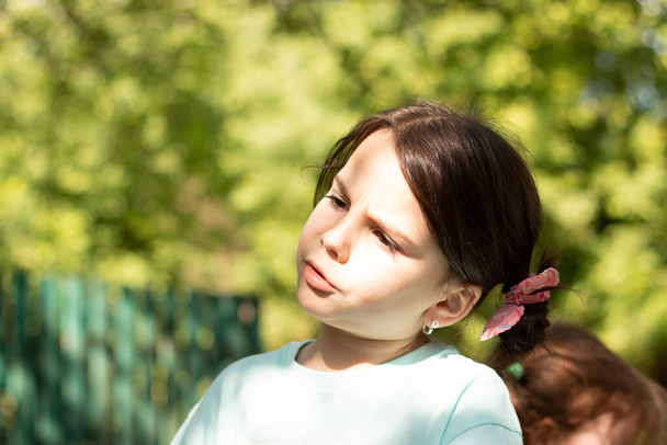 Μικρό όμορφο λευκό κορίτσι με μεγάλα μάτια κοιτάζει στο πλάι με συγκέντρωση σε ένα θολό ρουστίκ φόντο με bokeh - Φωτογραφία, εικόνα