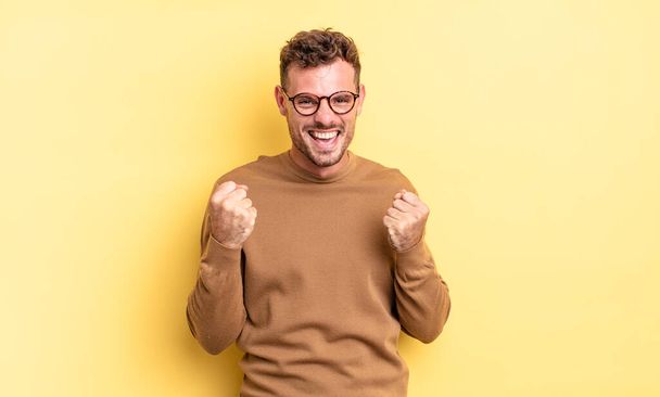 young handsome hispanic man shouting triumphantly, laughing and feeling happy and excited while celebrating success - Fotoğraf, Görsel