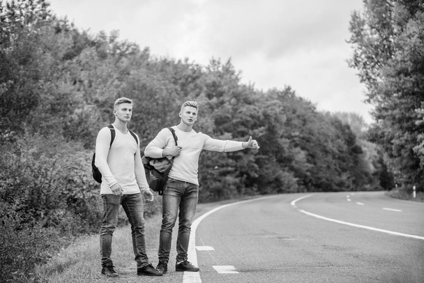type of adventure. On the road. Enjoying summer hike. Looking for transport. twins walking along road. stop car with thumb up gesture. hitchhiking and stopping car with thumbs up gesture - Foto, immagini