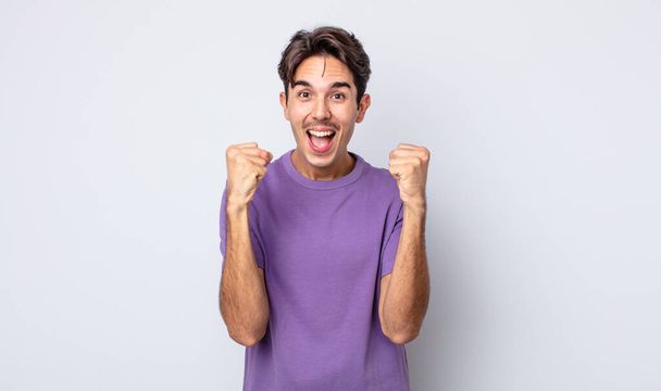 young handsome hispanic man feeling shocked, excited and happy, laughing and celebrating success, saying wow! - Photo, image