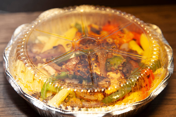 Grillezett csirke pirospaprikával és zöldpaprikás szeletekkel és karamellizált hagymával lezárt tárolóedényben. - Fotó, kép