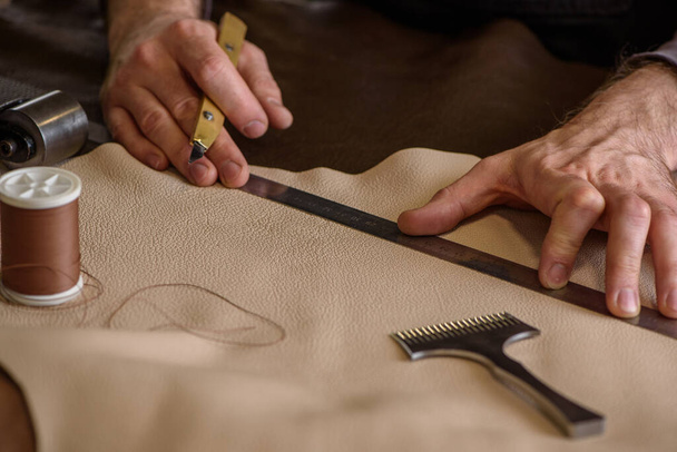 Les mains du cordonnier tenant un couteau artisanal préparant le cuir pour la coupe en atelier. Gros plan - Photo, image