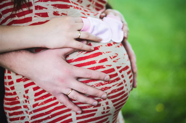 Close up man and woman holding woman's pregnant belly and the woman holding baby gloves in her hands - Foto, Imagen