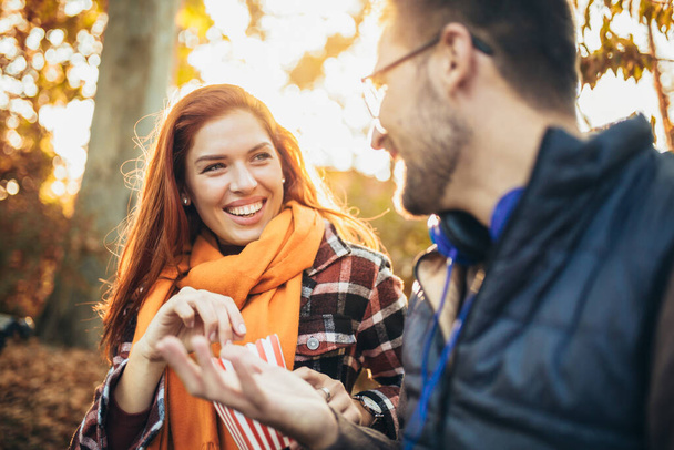 Bella giovane coppia seduta su una panchina nel parco autunnale a mangiare popcorn. - Foto, immagini