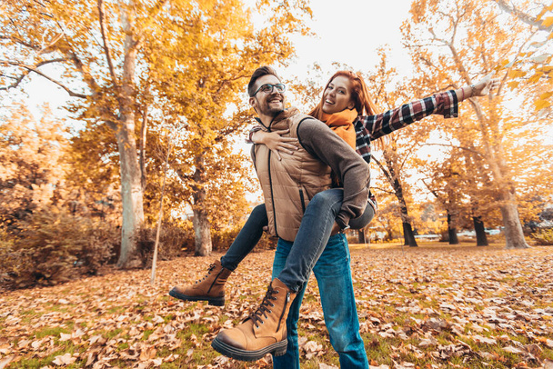 Smiling man carrying woman piggyback in autumn park. - Foto, Imagen