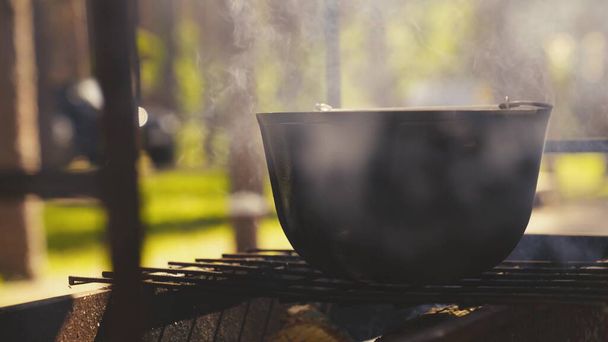 olla de cocina se encuentra en una rejilla con una gran llama de fuego, cocinar al aire libre en una cacerola, recetas turísticas al aire libre, plato de fuego los fines de semana, relajarse en el bosque - Foto, Imagen