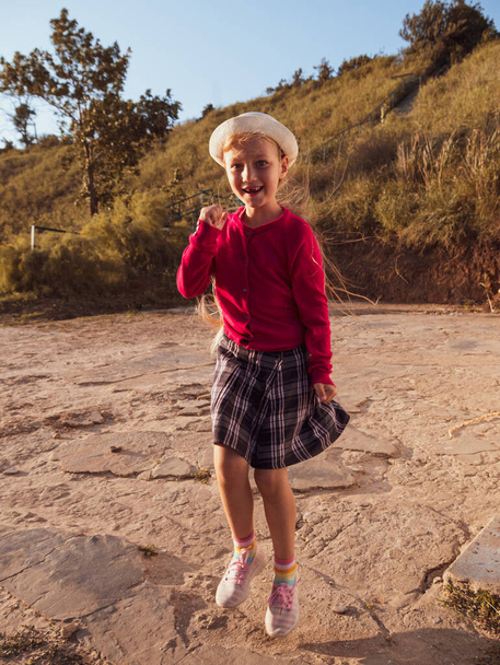 Onnellinen pieni tyttö pitkät hiukset muotokuva hyppäämällä luonnon taustalla tuulinen päivä. Söpö poika kävelee yksin syyspuistossa. Kaunis lapsi hattu lepää Matkustaa loma Vapaus elämäntapa onnea käsite - Valokuva, kuva