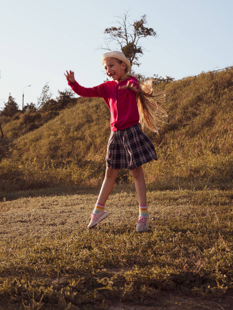 Счастливая маленькая девочка с длинными волосами, прыгающая на фоне природы в ветреный день. Симпатичный ребенок, гуляющий один в осеннем парке. Красивый ребенок в шляпе отдыхает Путешествия отпуск Свобода образ жизни счастье концепция - Фото, изображение