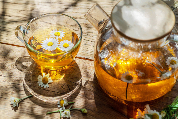 Herbal chamomile tea and chamomile flowers near teapot and tea glass. Top view. - Foto, afbeelding