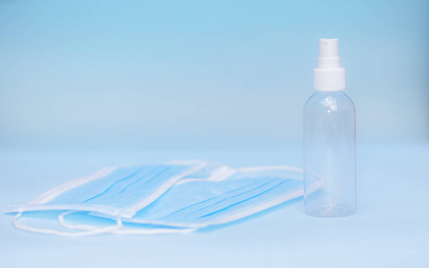 A closeup shot of a spray bottle and disposable facemasks on a light-blue background - Zdjęcie, obraz