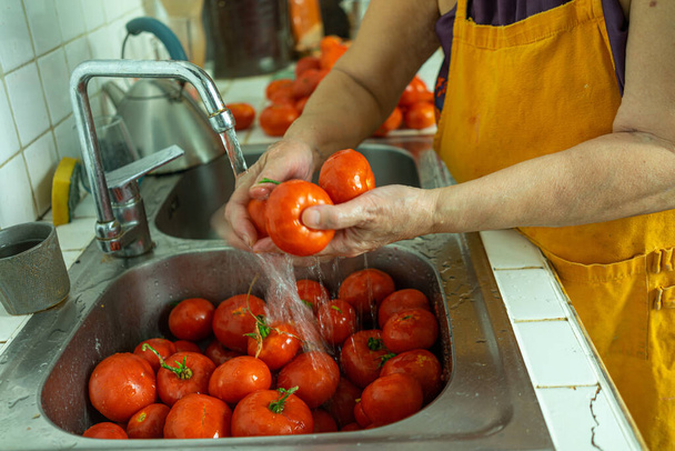A woman washing tomatoes for tomato sauce preparation - Фото, изображение
