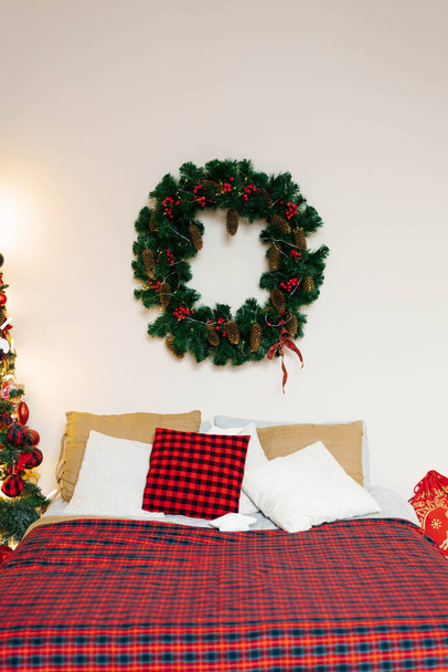 Een kerstkrans hangt boven het bed met een rode geruite deken in de slaapkamer - Foto, afbeelding