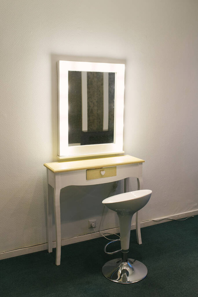 Ένα λευκό καθρέφτη μακιγιάζ και μια καρέκλα δίπλα του για μοντέλα και καλλιτέχνες - Φωτογραφία, εικόνα
