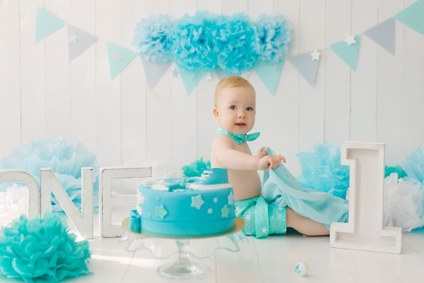 誕生日の子供1歳の男の子、青いガーランドとスーツと蝶ネクタイで座っている赤ちゃん - 写真・画像