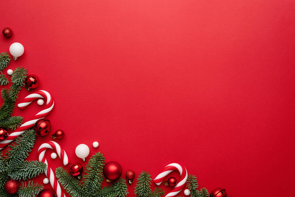 Fondo rojo con ramas de abeto, bastón de caramelo y adorno navideño para el diseño navideño. En blanco con un espacio de copia para texto - Foto, imagen
